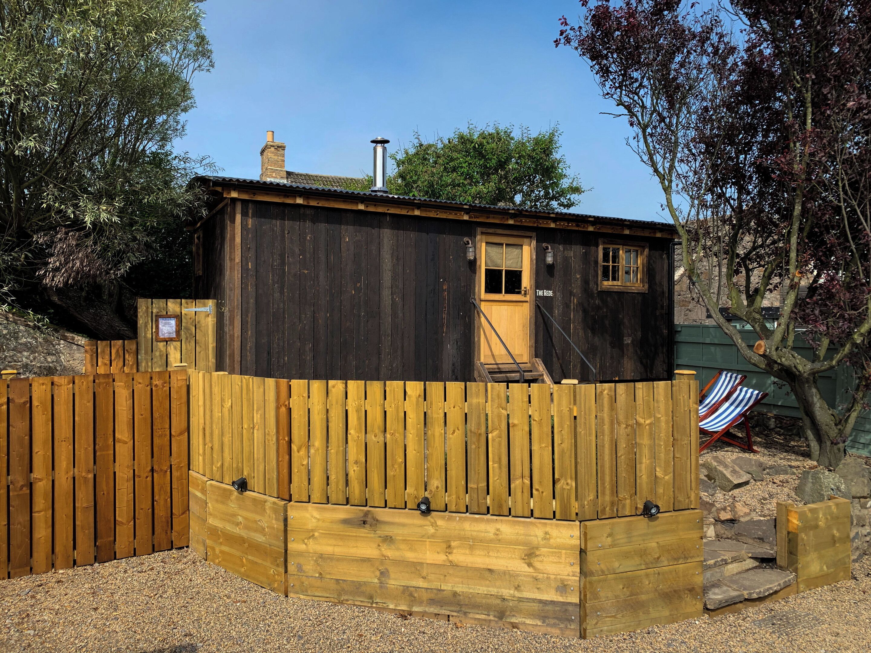 A wooden cabin with a wooden deck, a chimney, and a door labeled "THE REDE."
