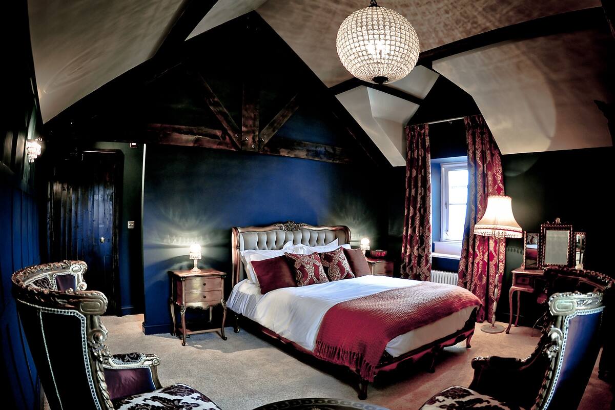 Une chambre à coucher avec un grand lit, un lustre, un bureau avec une lampe et une chaise.