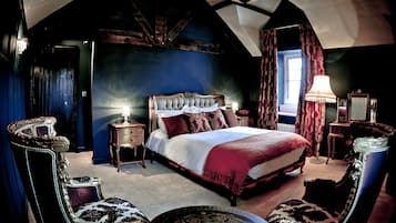 A bedroom with a large bed, a chandelier, a desk with a lamp, and a chair.