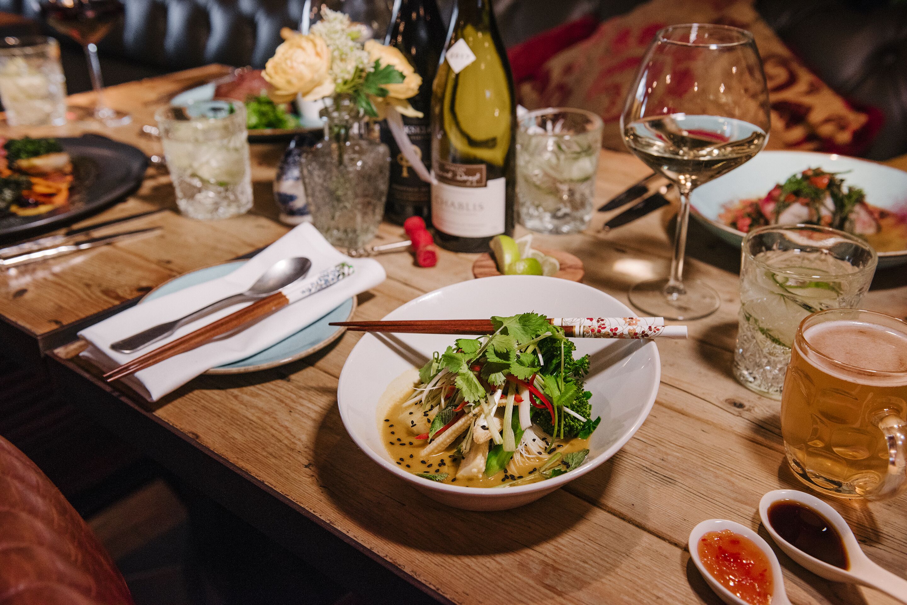 A dining table with a bowl of food, wine glasses, and a bottle of wine.