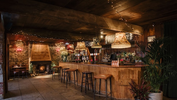 Un rústico bar con taburetes de madera, una chimenea de piedra y luces colgantes.