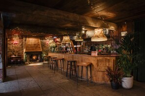 Un rústico bar con taburetes de madera, una chimenea de piedra y luces colgantes.