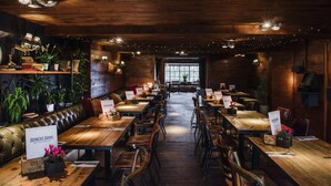 Un restaurante con mesas y sillas de madera, un banco de cuero y plantas en macetas.