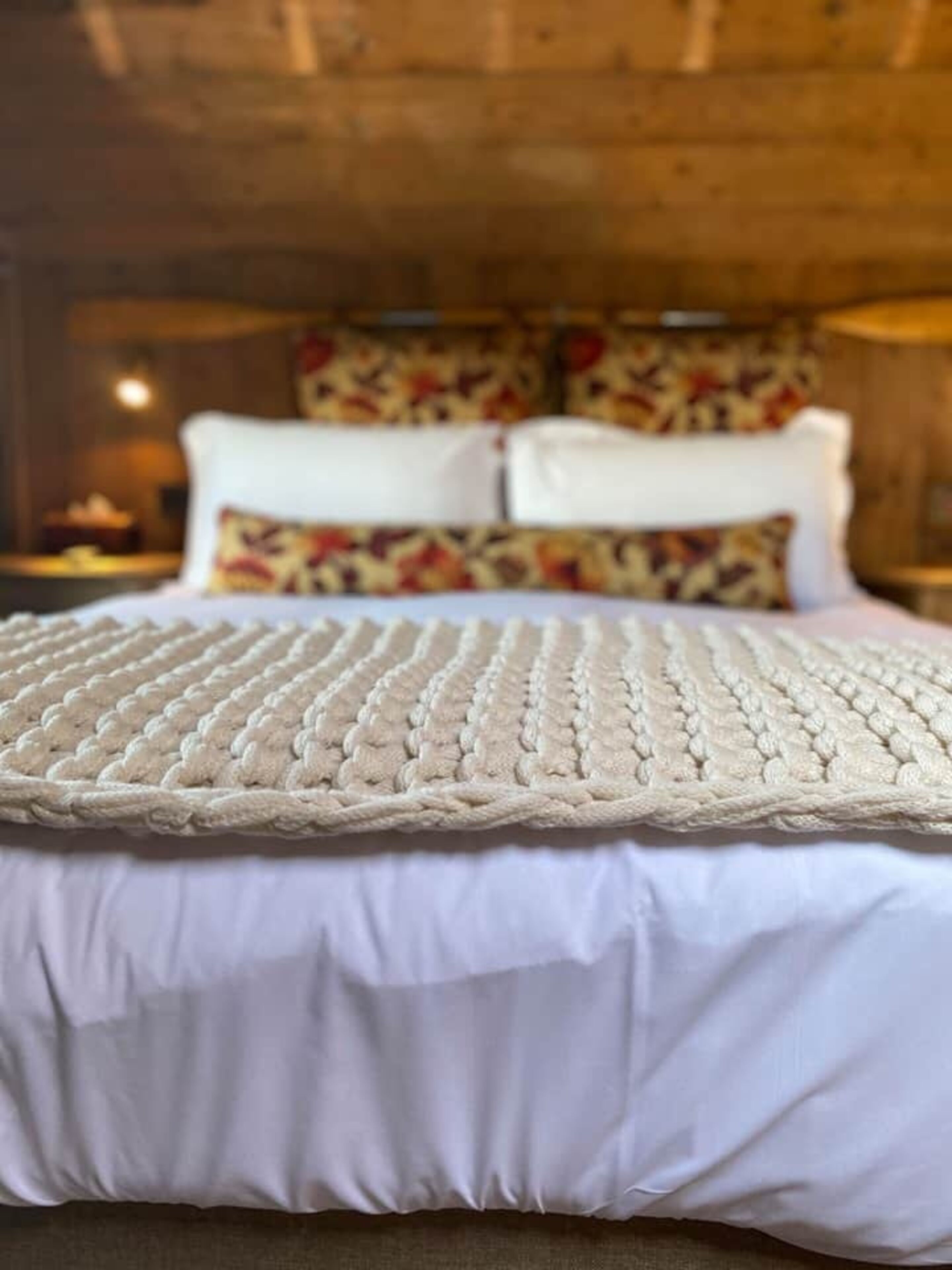 Ein Bett mit einer gewebten weißen Decke und einem gemusterten Kopfkissen.