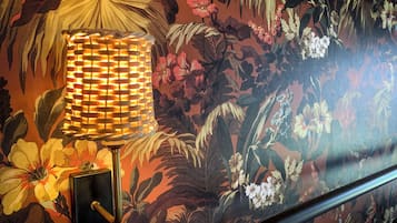 Una habitación con papel tapiz floral, una lámpara de pie y una barandilla de metal.