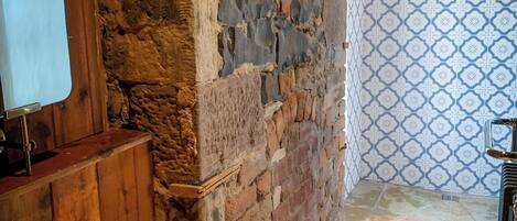 A bathroom with a stone wall, wooden vanity, copper basin, and patterned wall tiles.