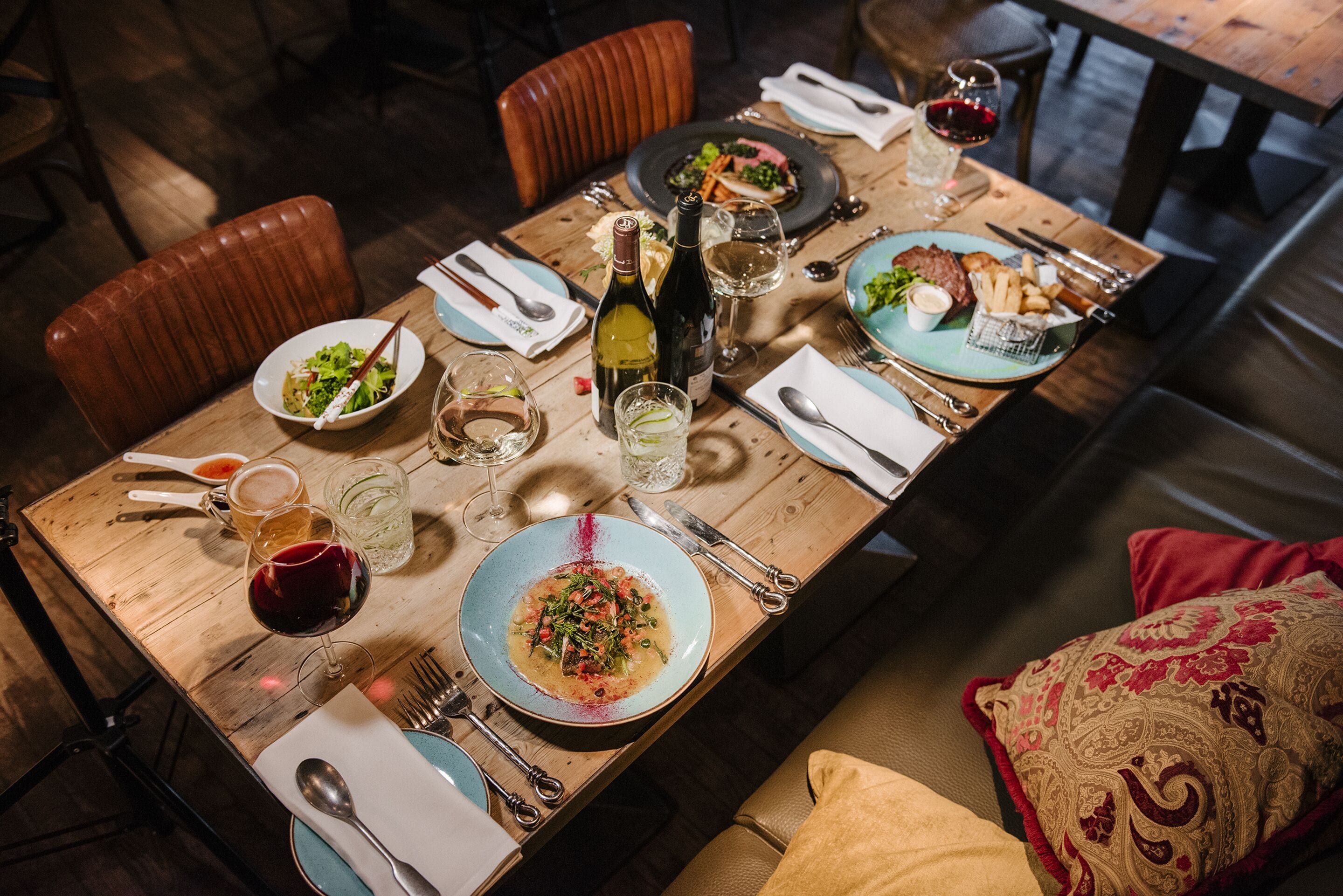 Une table de salle à manger en bois, mise avec des assiettes, des verres, des couverts et une bouteille de vin.