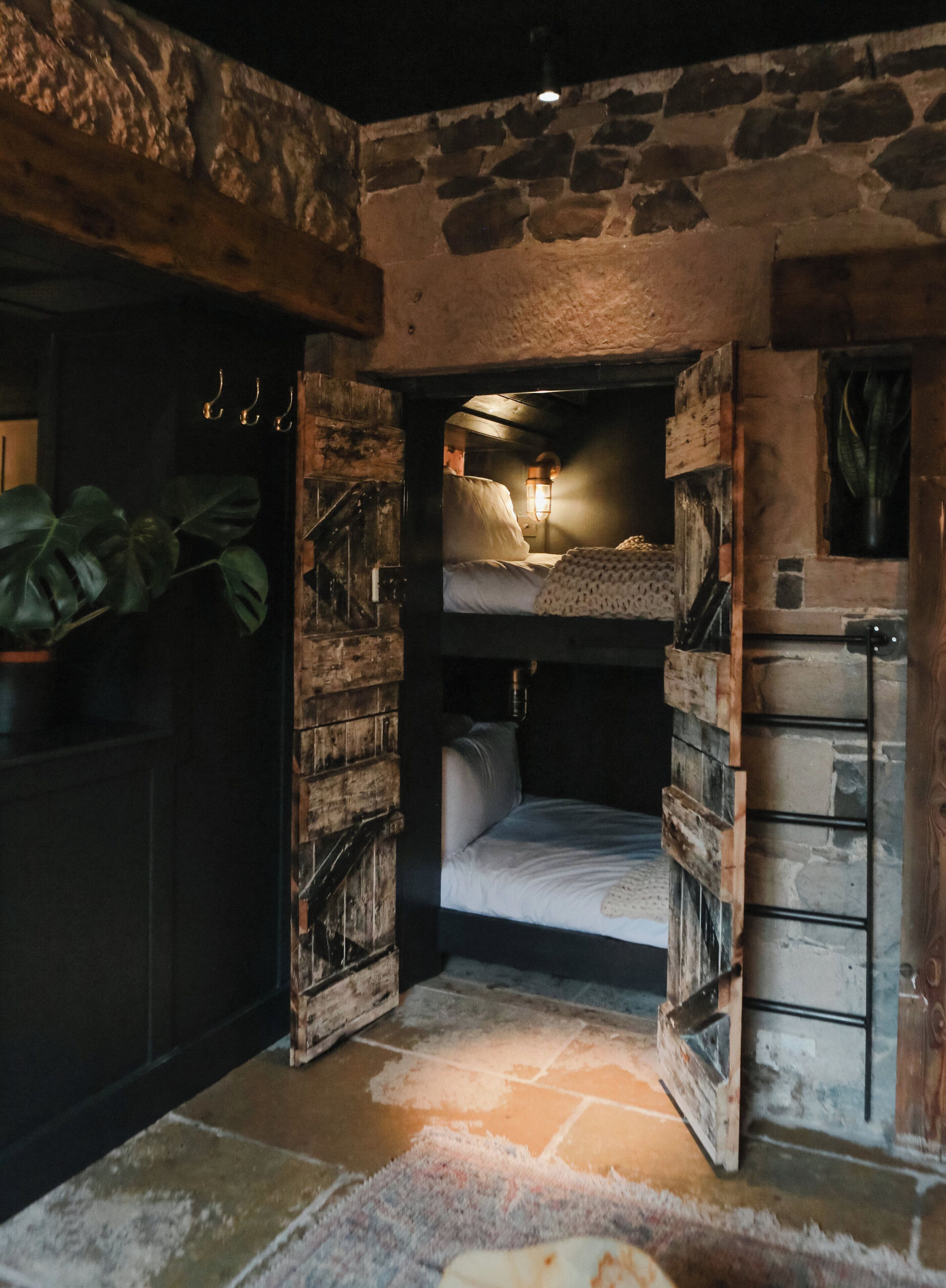 Una habitación rústica con una cama litera, paredes de piedra y un ventanal pequeño.