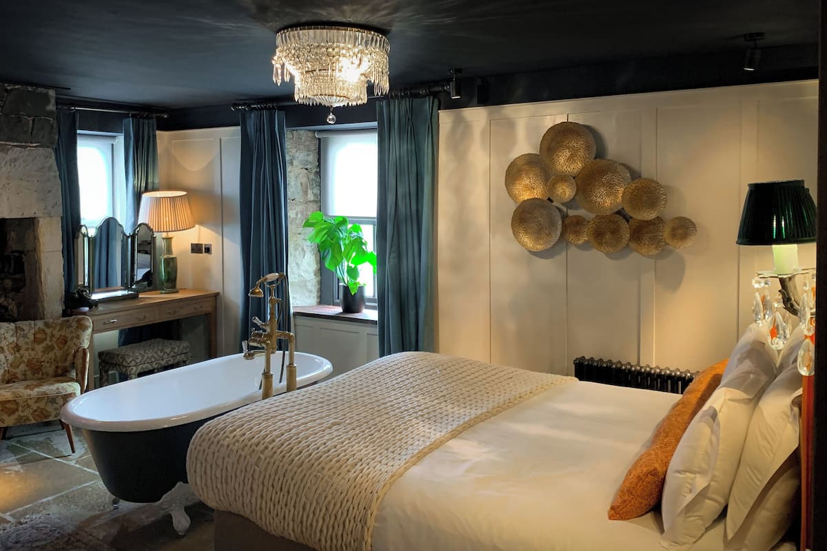 Une chambre à coucher avec un grand lit, une baignoire, une coiffeuse avec un miroir, un lustre et une plante.