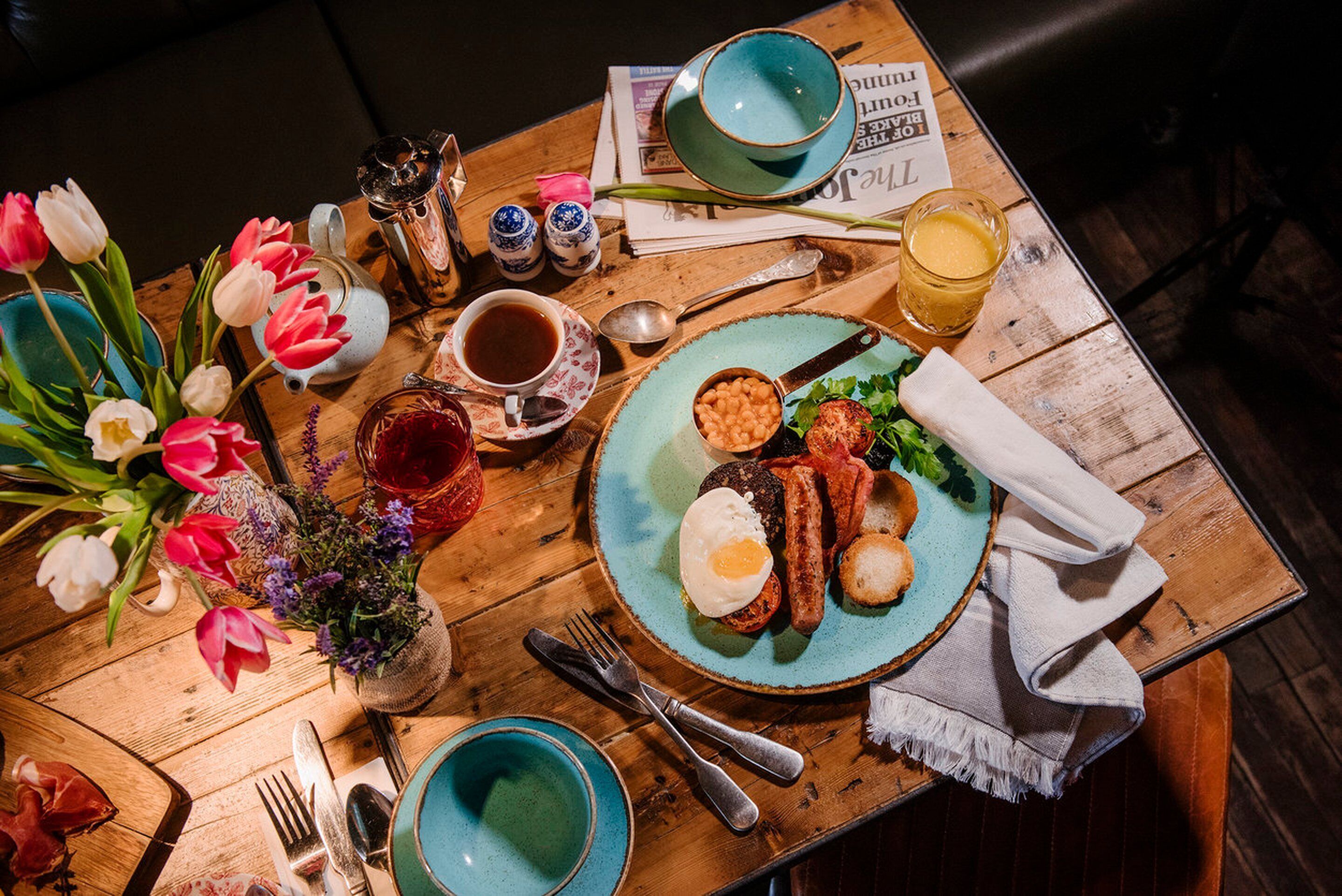 A wooden table with breakfast items, including eggs, sausages, and toast, along with a cup of coffee and a glass of orange juice.