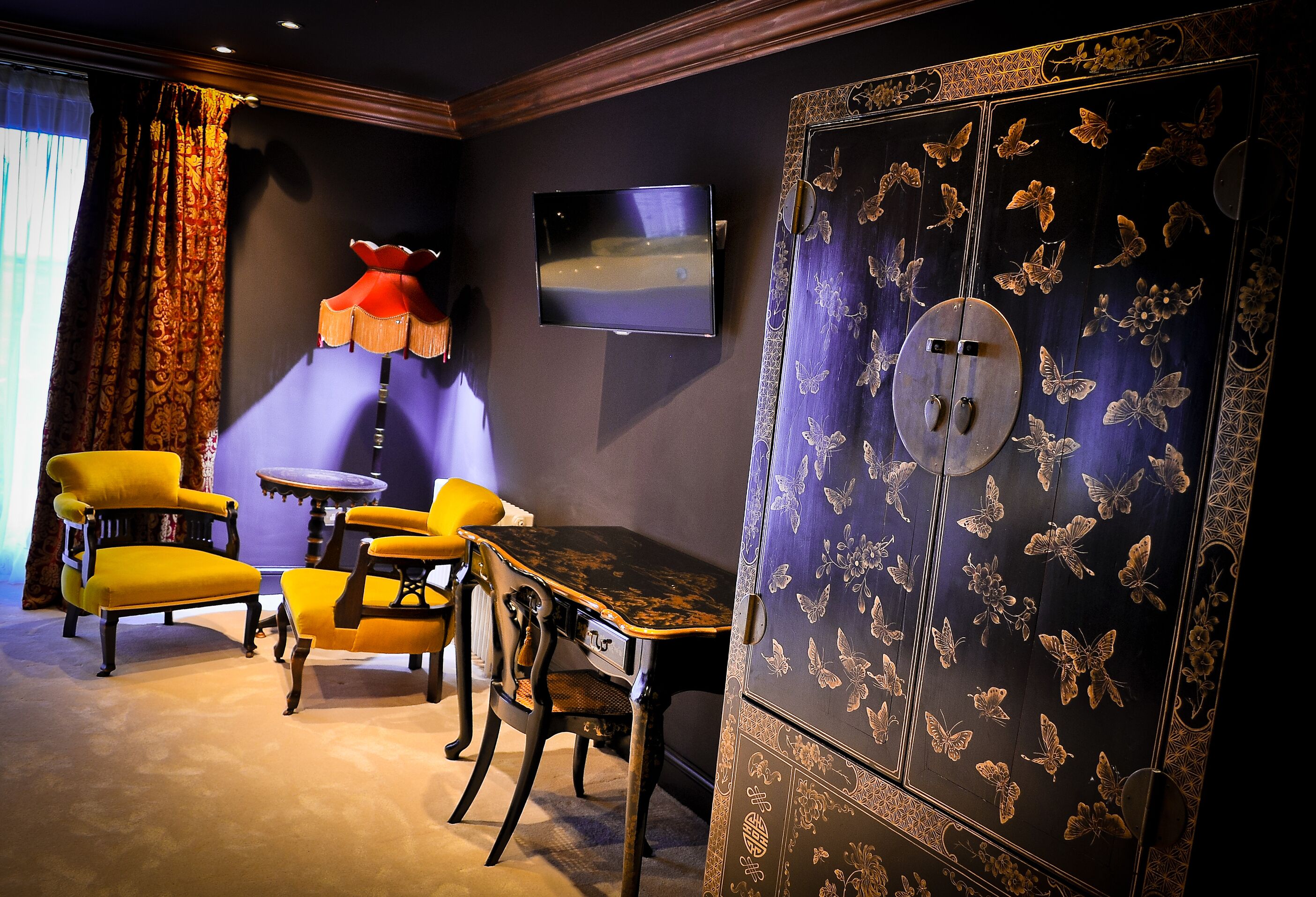 A room with a TV mounted on the wall, a table with chairs, and a large cabinet with butterfly designs.