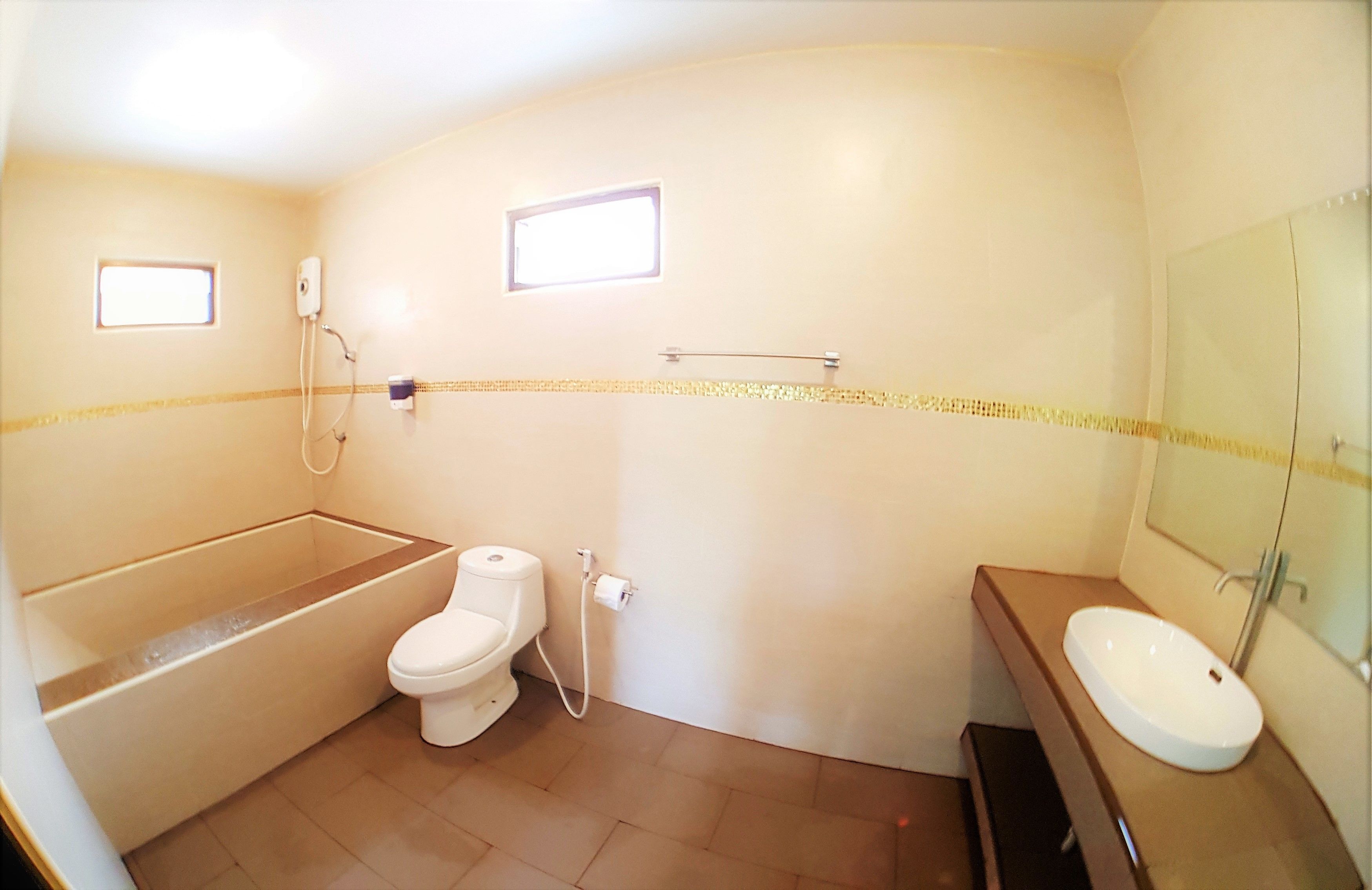 Ein kleines, kompaktes Badezimmer mit Toilette, Waschbecken und Badewanne. Zwei kleine Fenster und ein Spiegel befinden sich über dem Waschbecken.