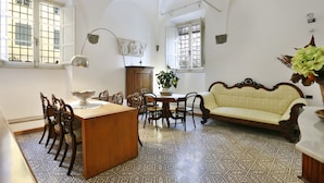 A dining area with a wooden table, chairs, and a central island. There is a sofa and a cabinet in the background. - B&B Pergola House (Lucca)