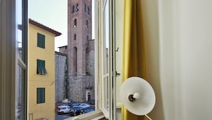 A window view of a narrow street with a historic brick tower, a yellow building, and parked cars. - B&B Pergola House (Lucca)