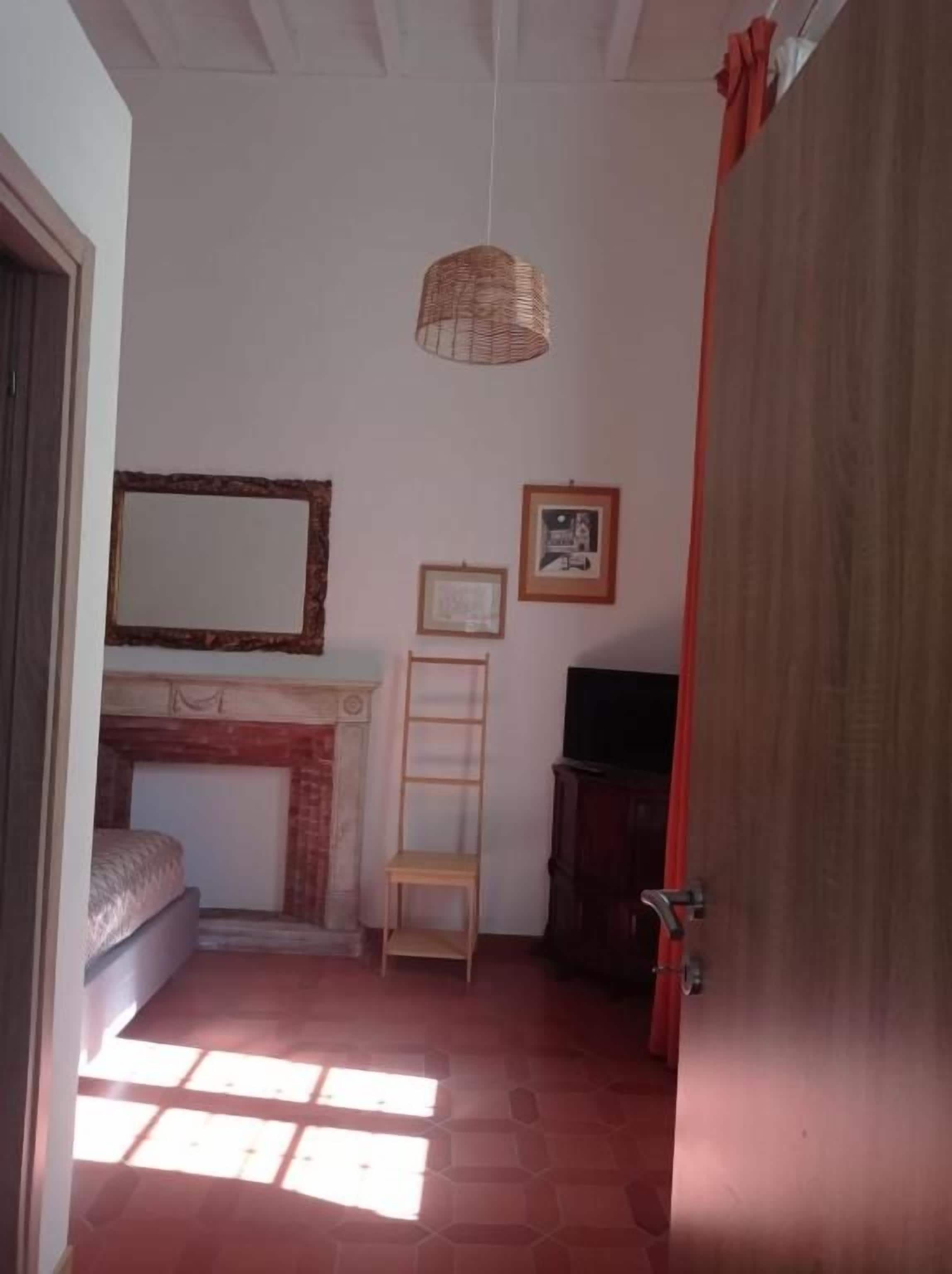 A room with a fireplace, a bed, a wooden ladder, a hanging light fixture, and a door.