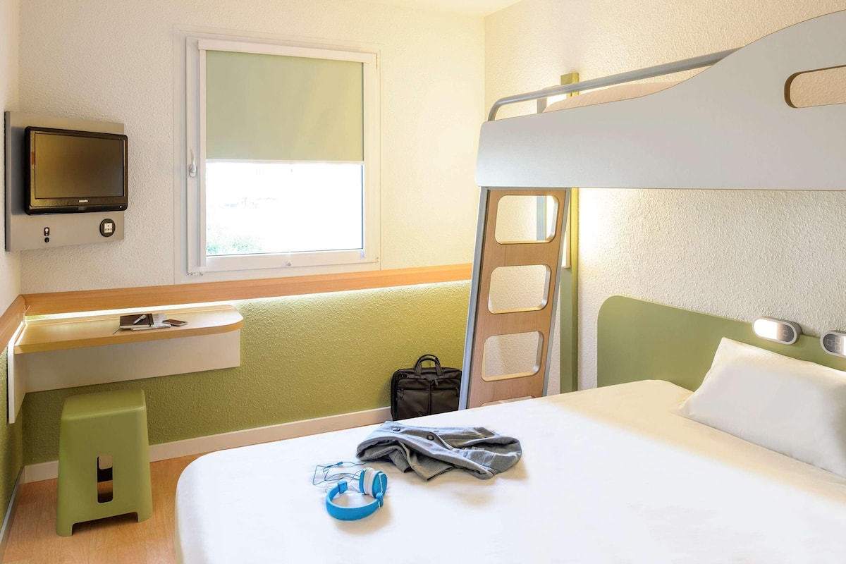 A bunk bed room with a television, a desk, and a window.