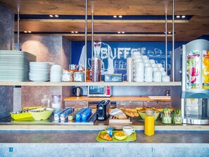 Ein Frühstücksbuffet mit verschiedenen Speisen, einer Kaffeemaschine und einer Tafel mit der Speisekarte.