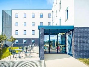 Ein modernes Gebäude mit überdachter Außenbestuhlung, einer Ziegel-Fassade und blauem Himmel.