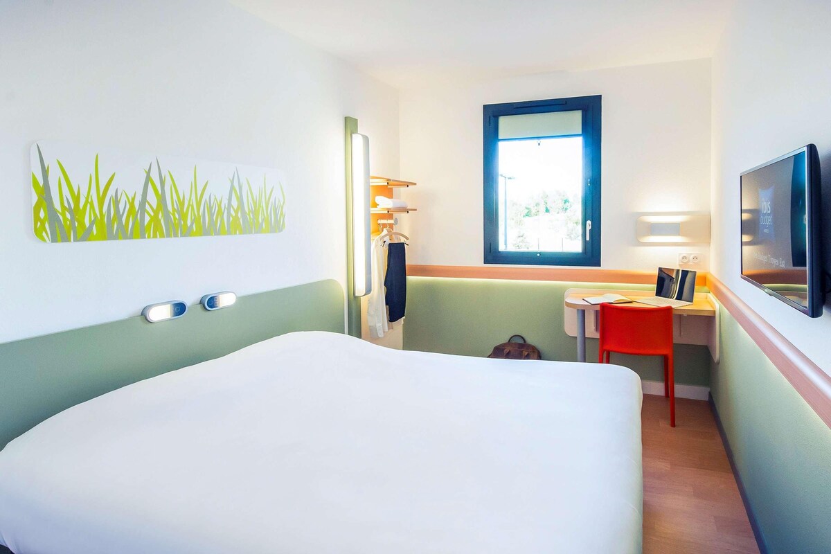 Ein Hotelzimmer mit Bett, Schreibtisch, Stuhl, Fernseher und Fenster.