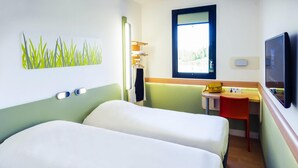 Ein Hotelzimmer mit zwei Betten, einem Schreibtisch, einem Stuhl, einem Fernseher und einem Fenster.