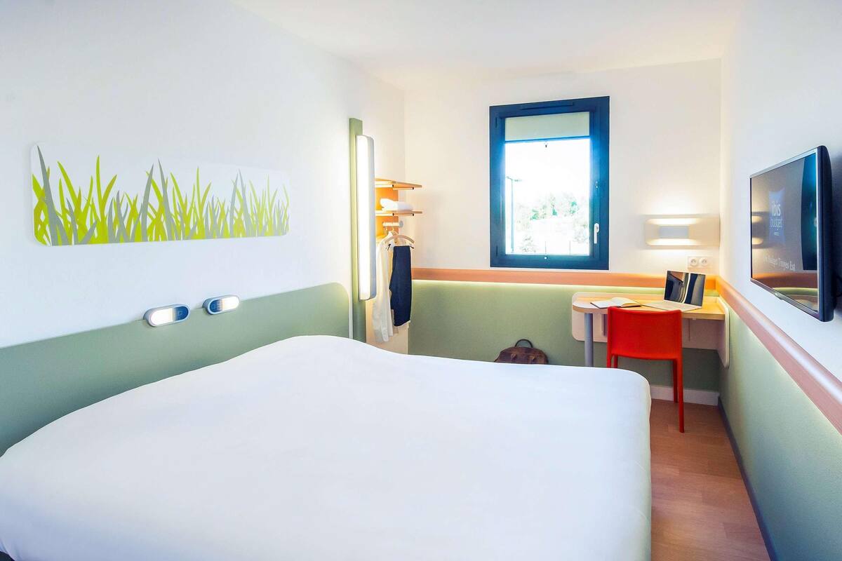 A hotel room with a bed, a desk, a chair, a TV, and a window.