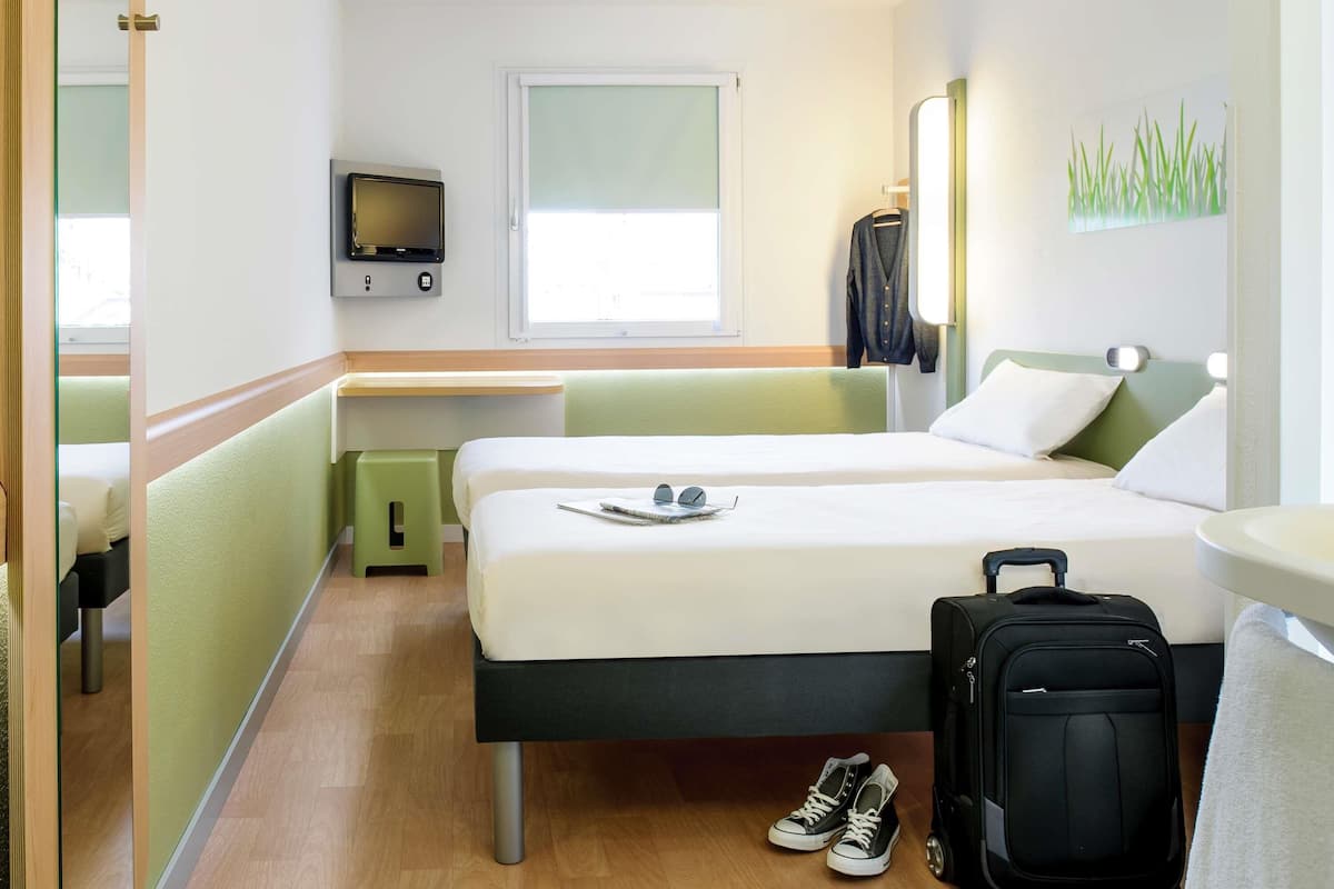 A hotel room with two beds, a TV, a window, and a suitcase.