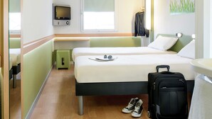 Ein Hotelzimmer mit zwei Betten, einem Fernseher, einem Fenster und einem Koffer.