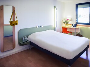 Une chambre d’hôtel comprenant un lit, une table de chevet, un miroir, un bureau, une chaise et une fenêtre.