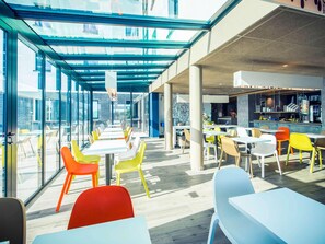Un espace repas moderne avec des murs en verre, des chaises colorées et un comptoir de bar.