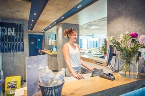 Ein Empfangstisch mit Computer, Kasse, Blumenvase und einer Pinnwand mit einer Kreidetafel.