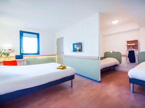 Ein Hotelzimmer mit zwei Betten, einem Schreibtisch mit Stuhl, einem Fernseher und einem Fenster.