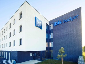 Ein modernes Hotelgebäude mit einem auffälligen 'ibis budget'-Schild, einer sauberen Fassade und einem gepflegten Eingangsbereich.