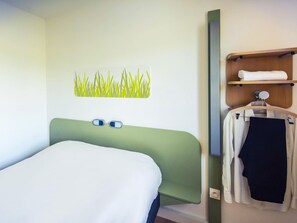 Una habitación de hotel con una cama, un toallero de pared y una pequeña estantería con una toalla.