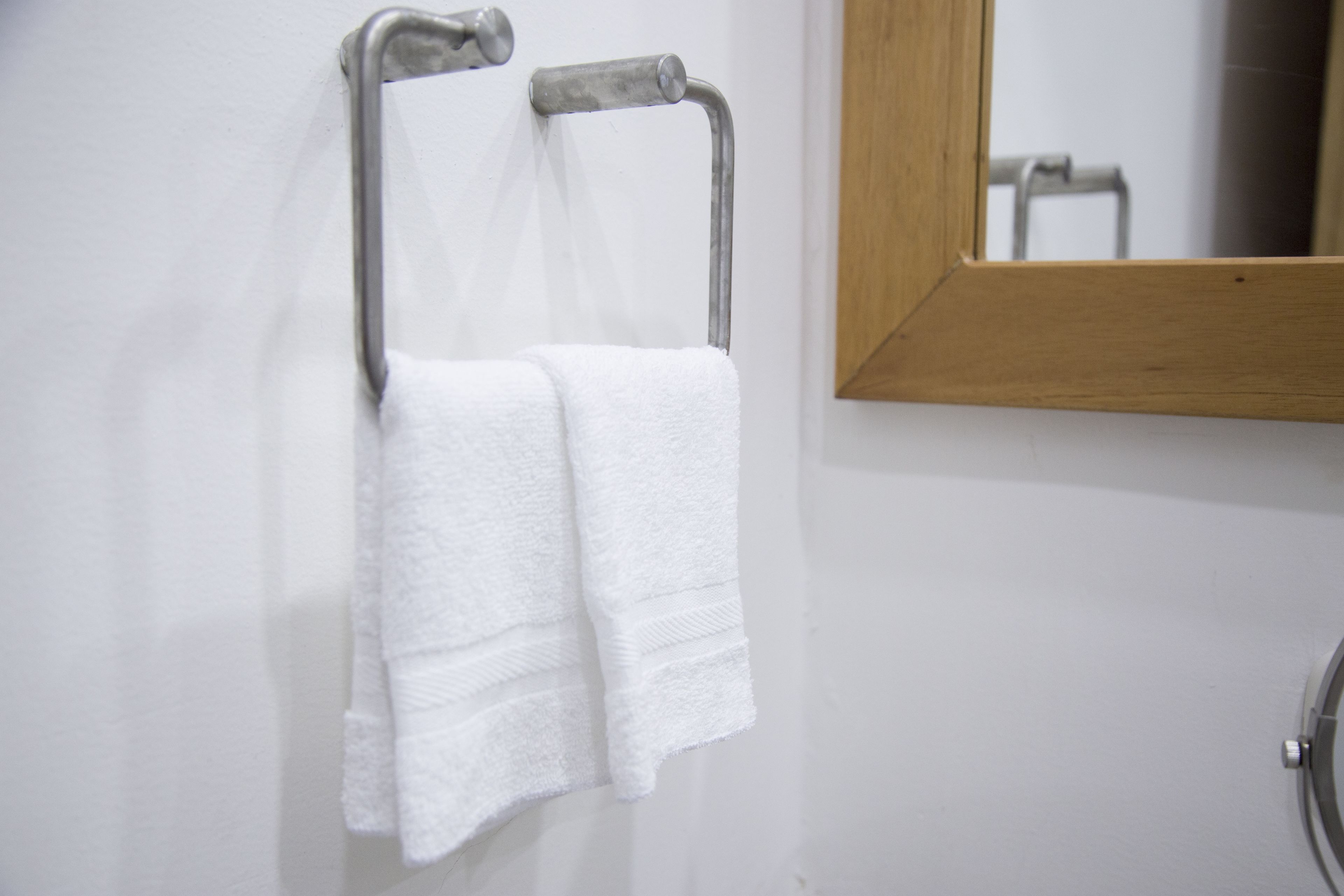 A white towel hanging on a metal towel rack in a bathroom with a wooden-framed mirror.