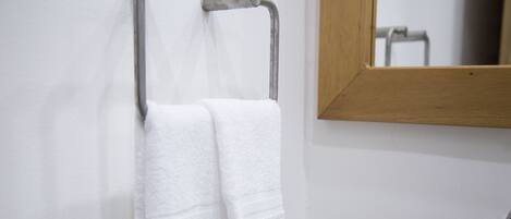 A white towel hanging on a metal towel rack in a bathroom with a wooden-framed mirror.