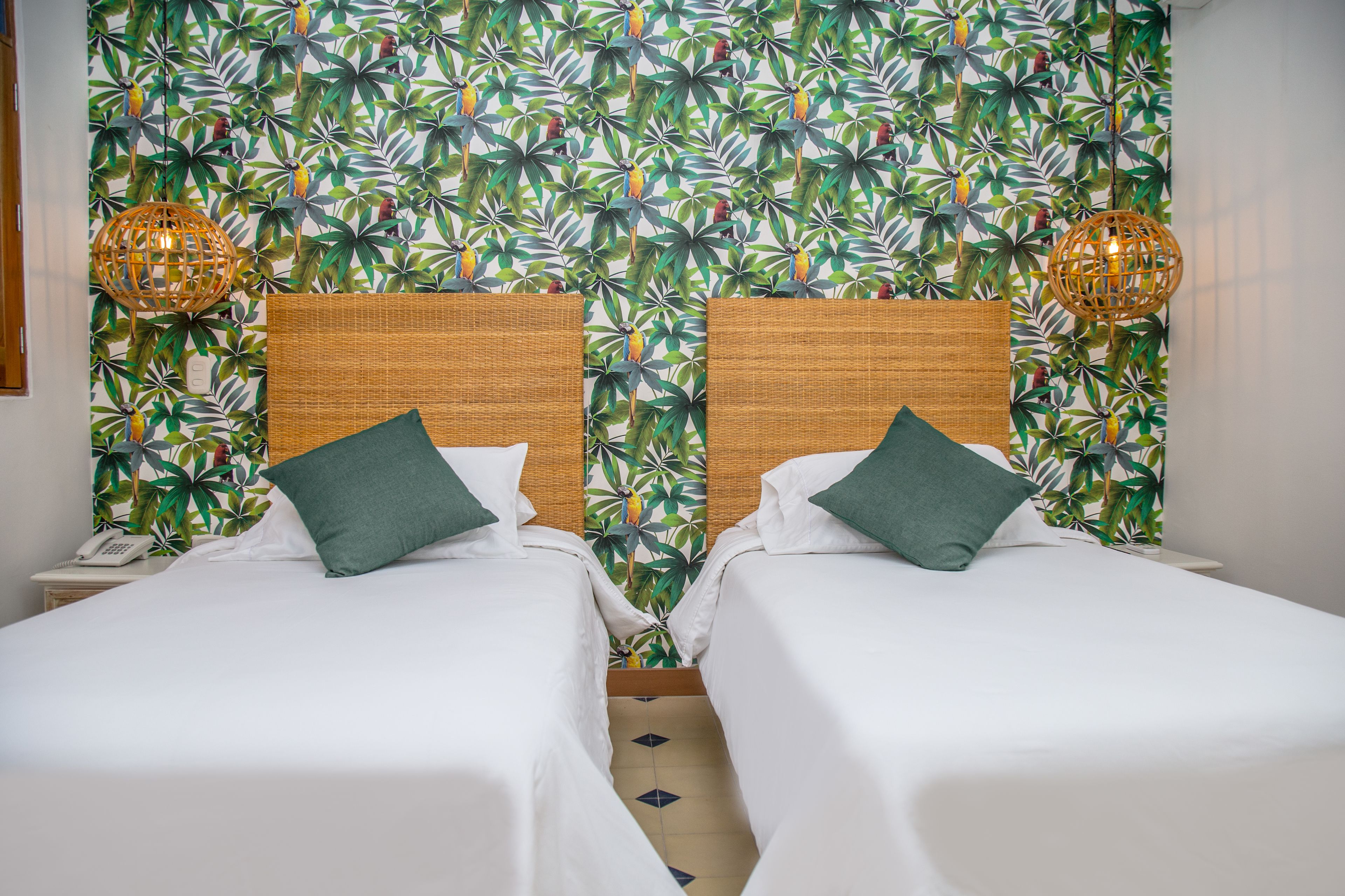 Habitación de hotel con dos camas individuales, papel tapiz estampado y dos lámparas de mimbre.