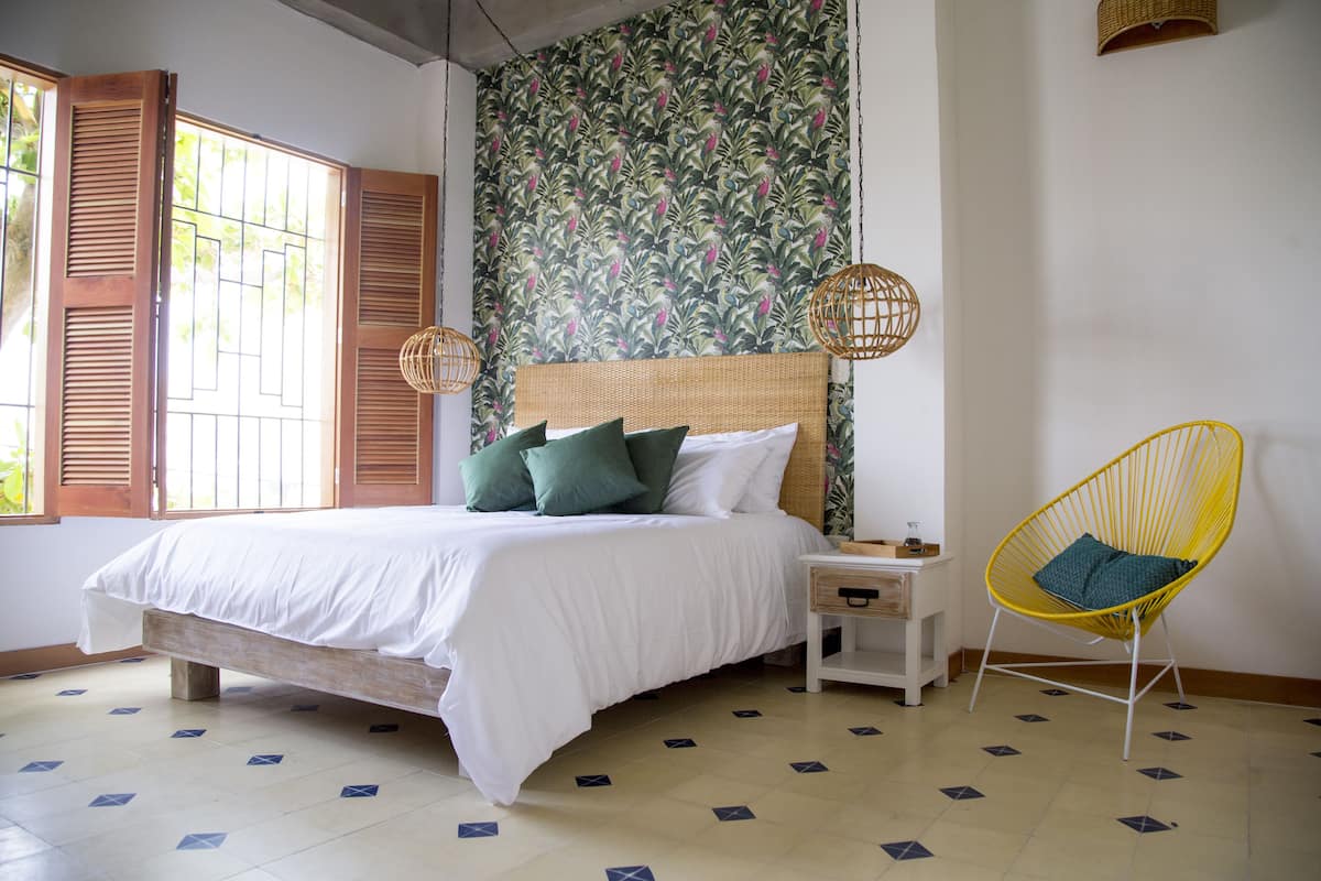 Une chambre à coucher comprenant un lit, une table de chevet, une chaise et un mur orné d’un motif floral.