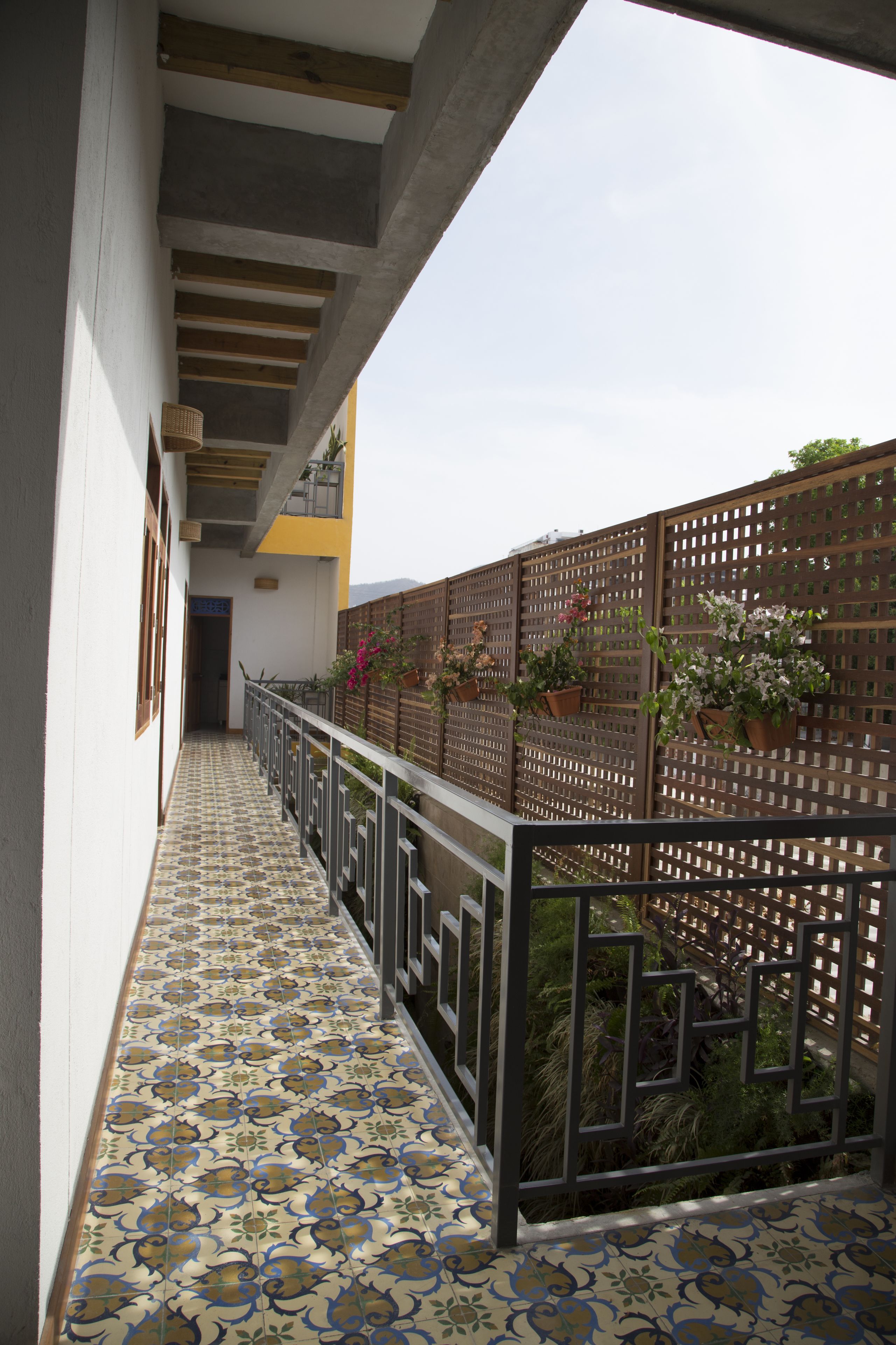 A narrow corridor with patterned floor tiles, a metal railing, and potted plants on a wooden fence.