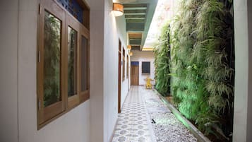 Um corredor estreito com piso de azulejos, portas de madeira e um jardim vertical em uma das paredes.