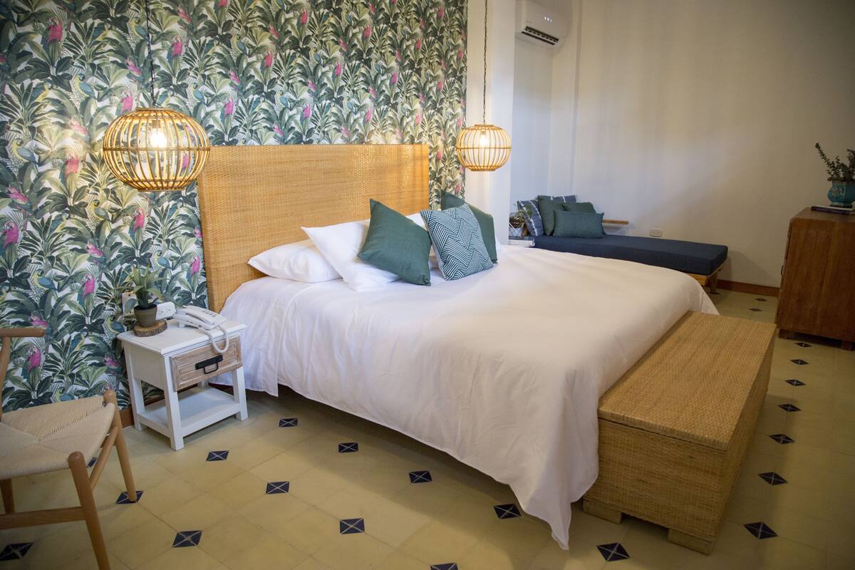 Une chambre à coucher bien aménagée, avec un grand lit, des tables de chevet, une petite table de chevet avec une lampe et un banc.