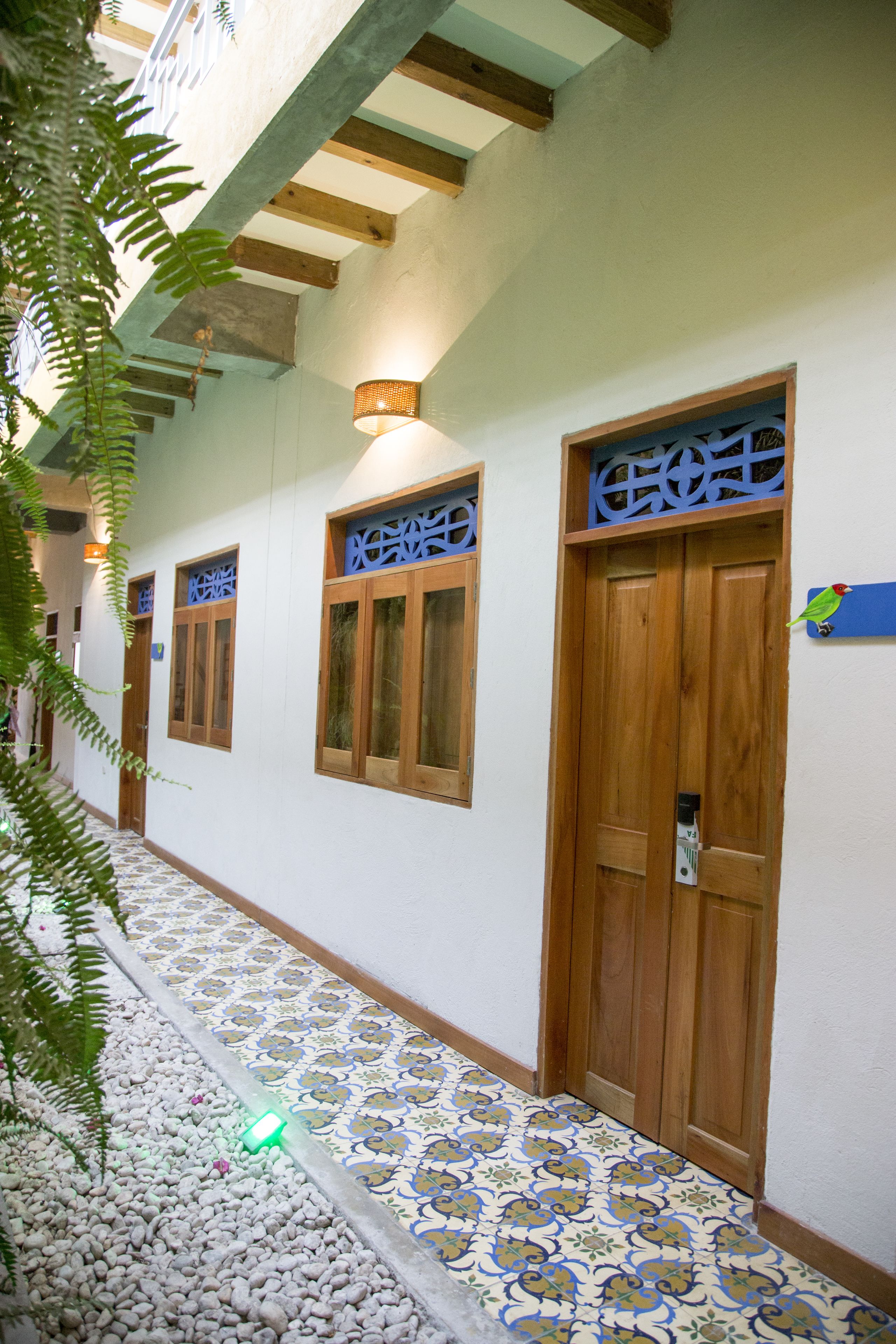 A corridor with patterned floor tiles, wooden doors, and windows with blue signage.
