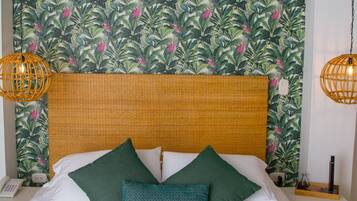 Una cama bien tendida con sábanas blancas y almohadas verdes, un cabecero de mimbre y un estampado de papel tapiz tropical.