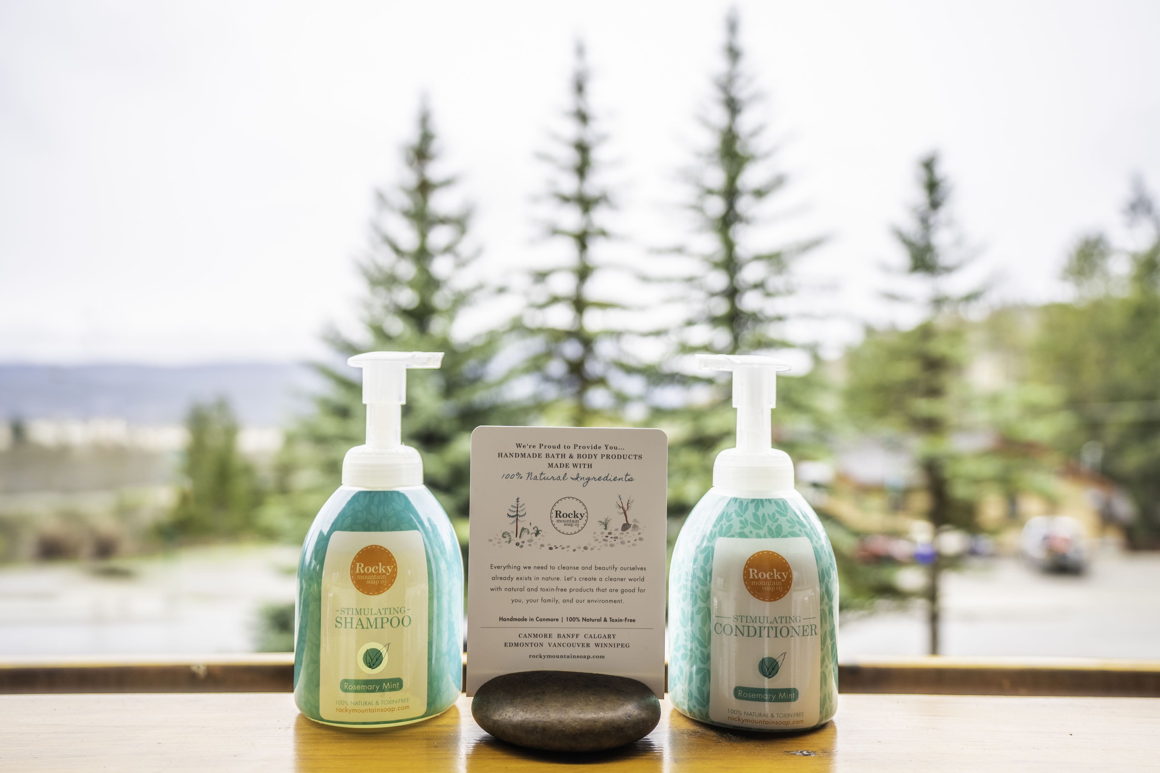 Deux bouteilles de produits de la marque Rocky Mountain Spa, une table en bois et une fenêtre donnant sur des arbres et une route.