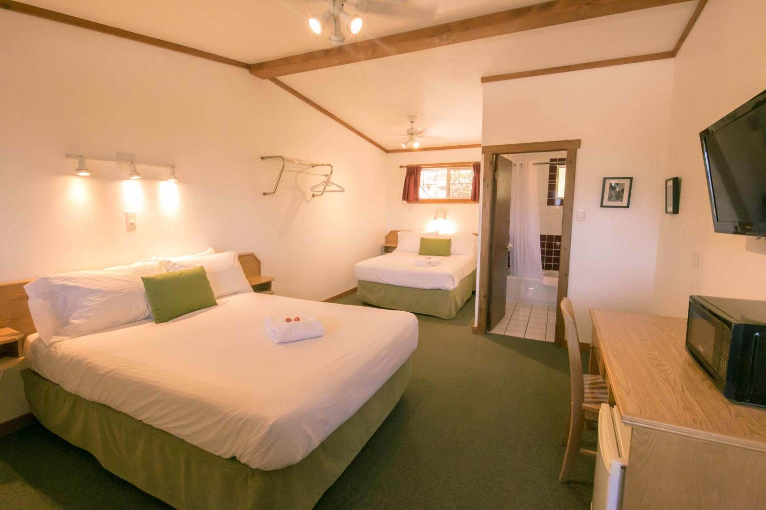 Hotellihuone, jossa on kaksi sänkyä, puinen työpöytä, televisio ja kattotuuletin.