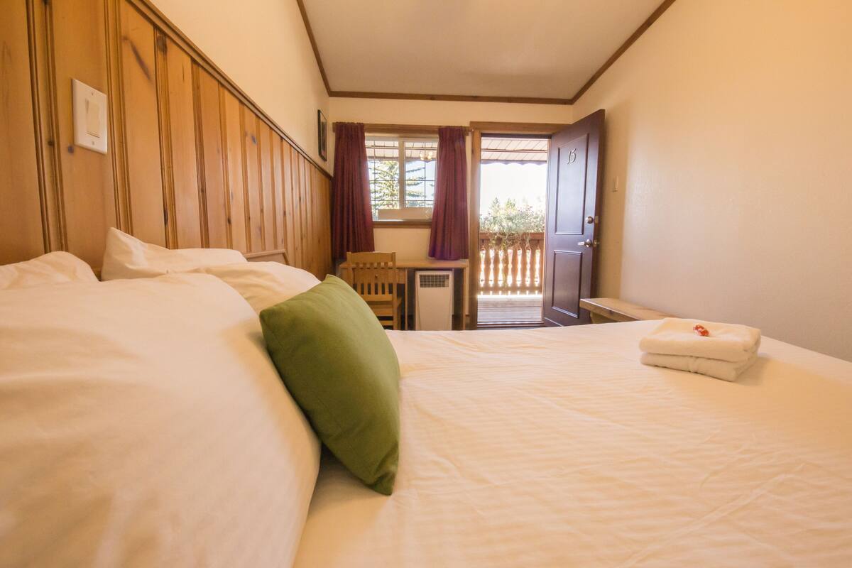 A hotel room with a bed, a desk, and a window with curtains.