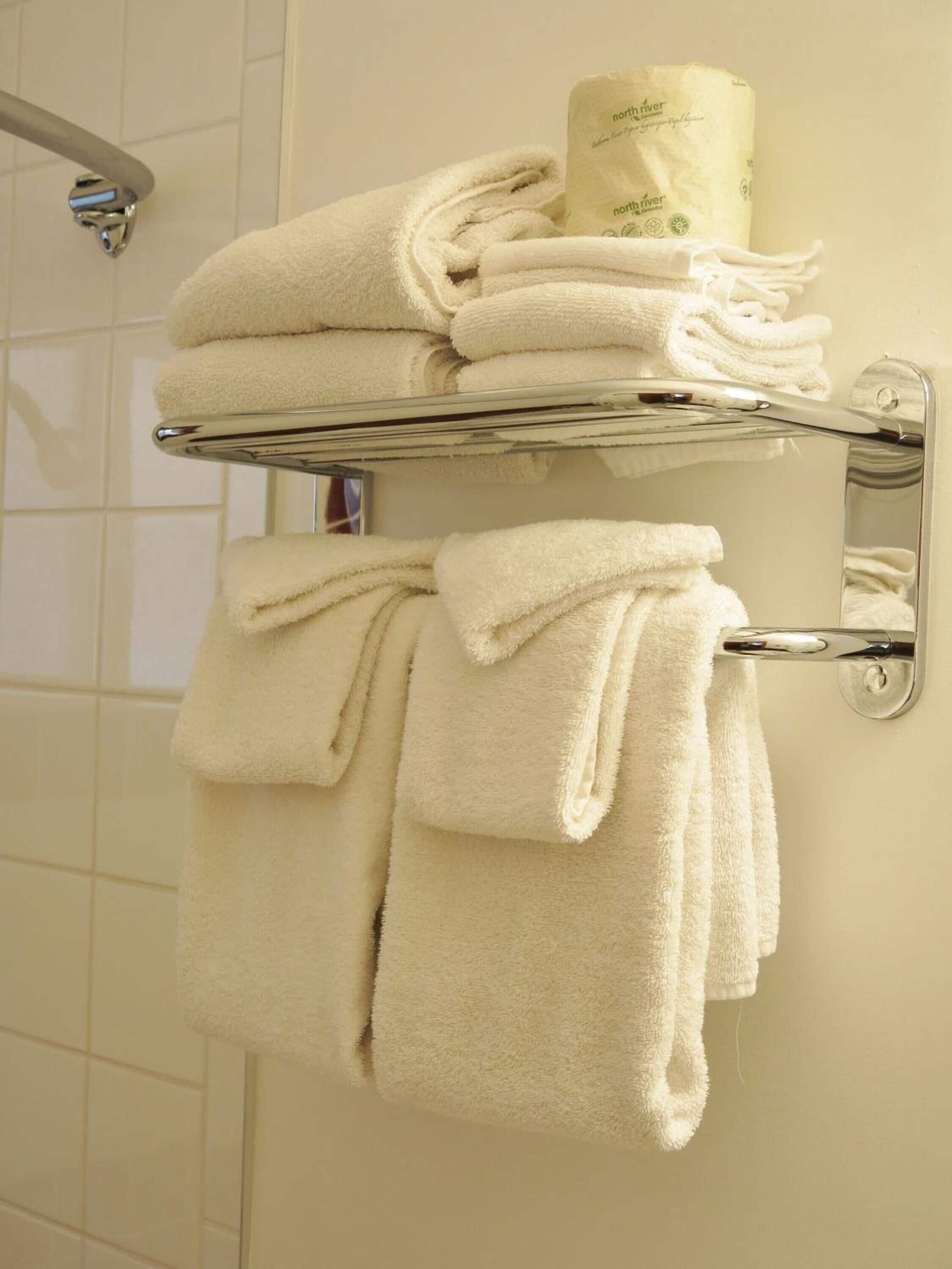 Un baño con un perchero con toallas dobladas y un rollo de papel higiénico.