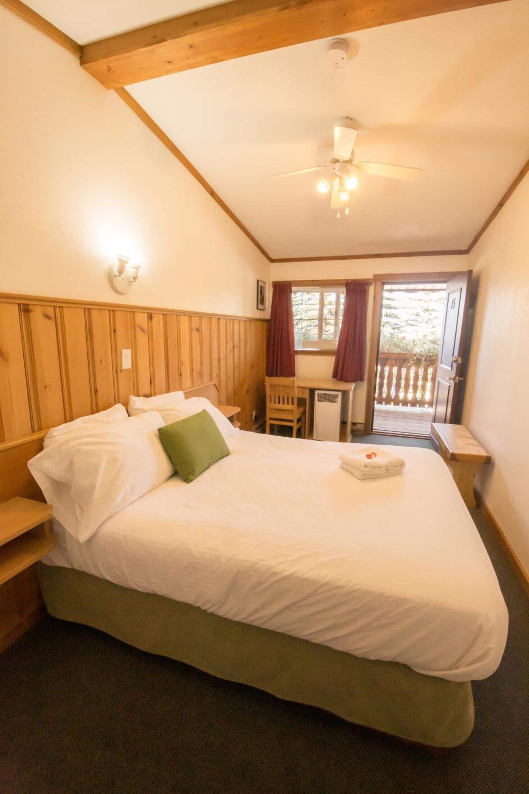 Ein Schlafzimmer mit Bett, Schreibtisch und Stuhl. Ein Fenster mit Vorhängen und eine Tür zu einem Außenbereich.