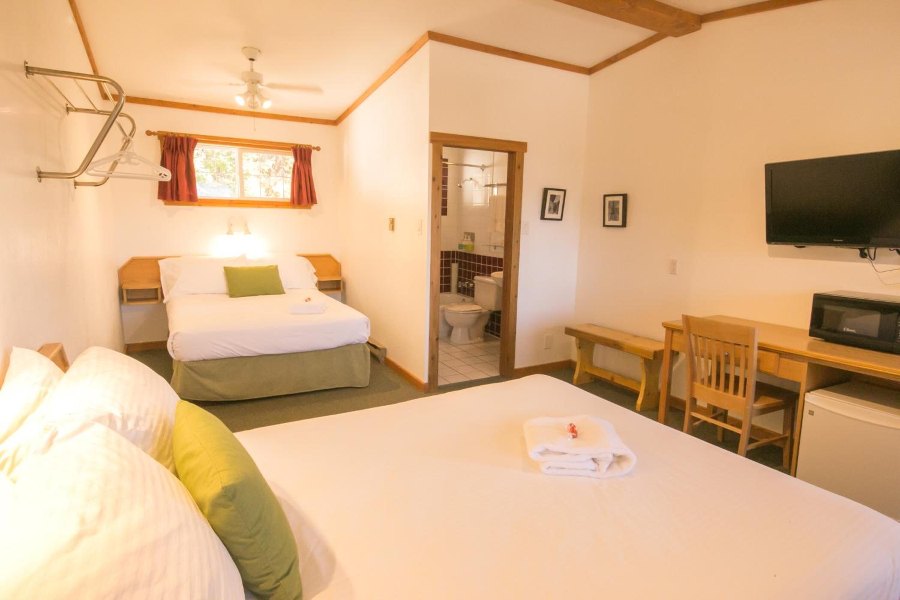 Habitación de hotel con cama, escritorio, televisor y baño visible a través de una puerta abierta.