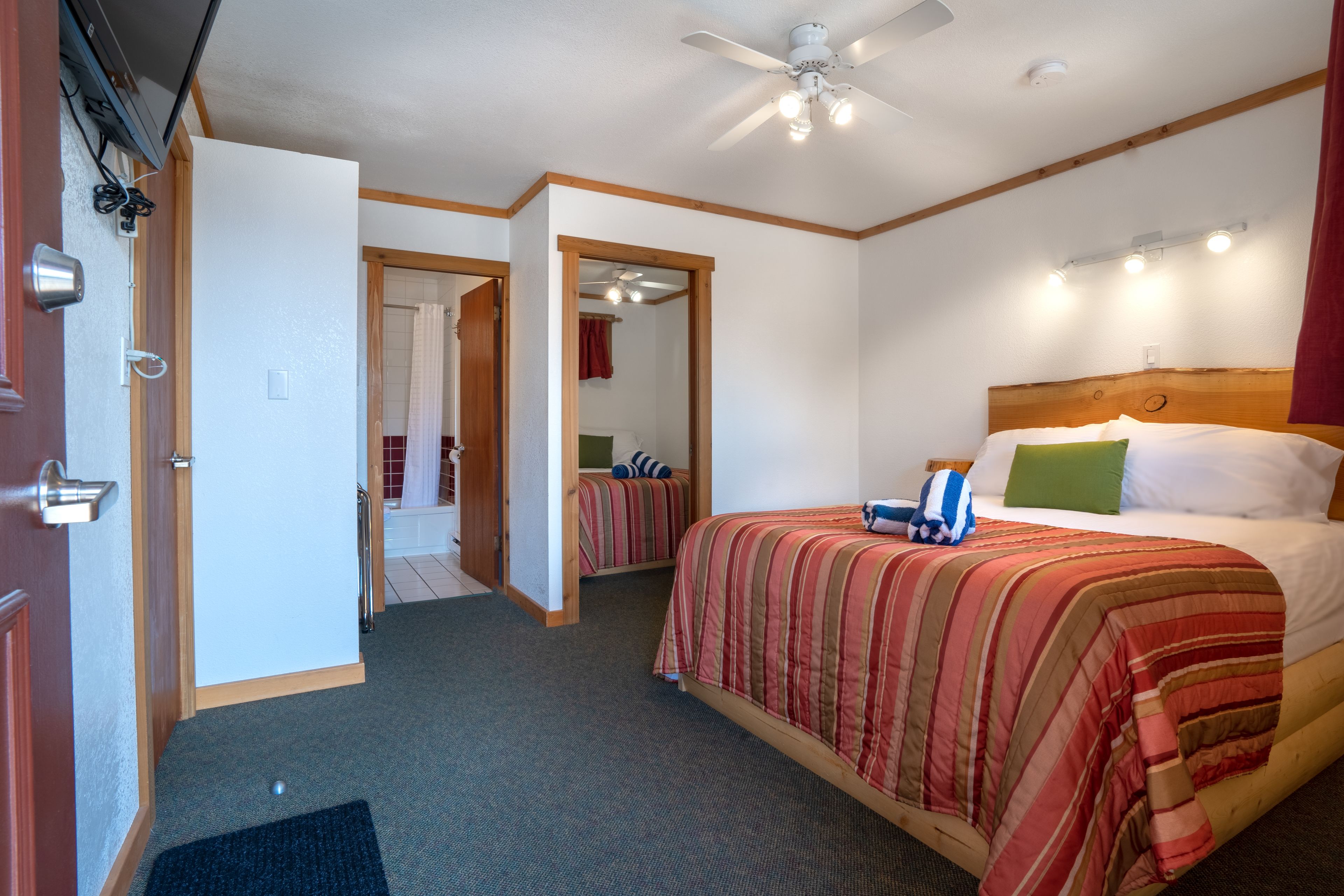 Une chambre d’hôtel avec un lit, un ventilateur de plafond, une porte et un couloir menant à une autre chambre.