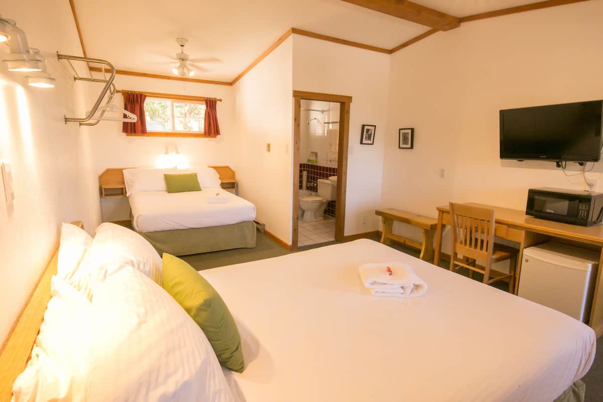A hotel room with a large bed, a desk with a chair, a television, and a small refrigerator.